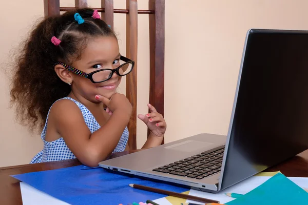 Chica pequeña multirracial divertida con gafas y el uso de un ordenador portátil —  Fotos de Stock