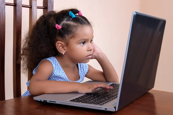 Mnohonárodnostní malá dívka použití přenosného počítače v domácnosti — Stock fotografie