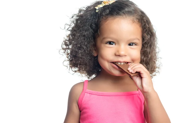 Joyful little girl with an afro hairstyle eating a chocolate bar — Stock Photo, Image