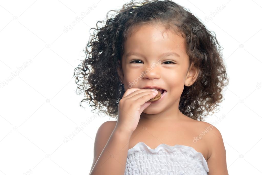 Joyful little girl with an afro hairstyle eating a chocolate cookie