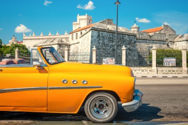 Vintage car parked next to an old castle in Havana clipart