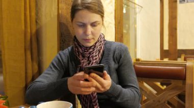 Bir telefonda App kullanarak ve kahve içme ve kafede gülümseyen genç kadın. 4k Uhd