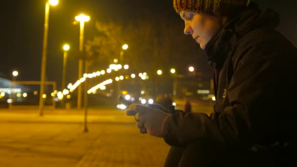 Dziewczyna wih telefonem w ręce. Pogaduchy na tle miasta w nocy. 4k wideo. — Wideo stockowe
