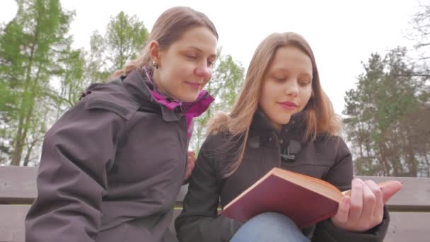 Madre e figlia leggono un libro in un parco e conversano. 4K UHD — Video Stock