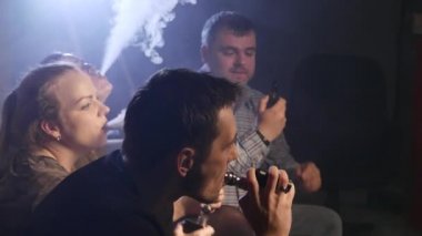 Bir grup insanlar vaping, teneffüs edilmesi ve büyük bulutlar duman exhaling ve birlikte eğlenmek. İyi arkadaş şirket. 4k Uhd.
