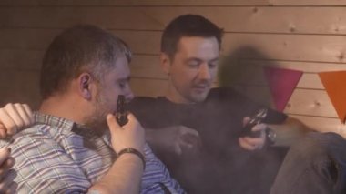 Bir grup insanlar vaping, teneffüs edilmesi ve büyük bulutlar duman exhaling ve birlikte eğlenmek. İyi arkadaş şirket. 4k Uhd.