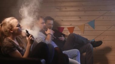 Bir grup insanlar vaping, teneffüs edilmesi ve büyük bulutlar duman exhaling ve birlikte eğlenmek. İyi arkadaş şirket. 4k Uhd.