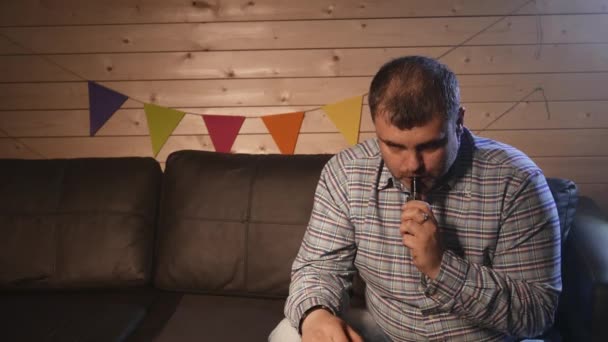 Un uomo seduto su un divano a vaporizzare sigarette elettroniche. 4K UHD — Video Stock