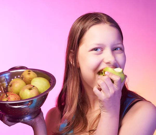 Adolescente segurando um escorredor cheio de maçãs e comendo uma maçã — Fotografia de Stock