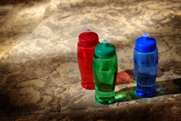 Botellas de agua rojas, verdes y azules en rocas ásperas — Foto de Stock