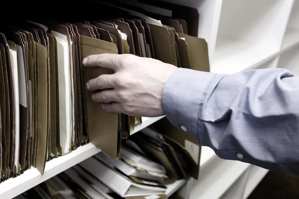Empresário Alcançando a mão para arquivos na prateleira — Fotografia de Stock