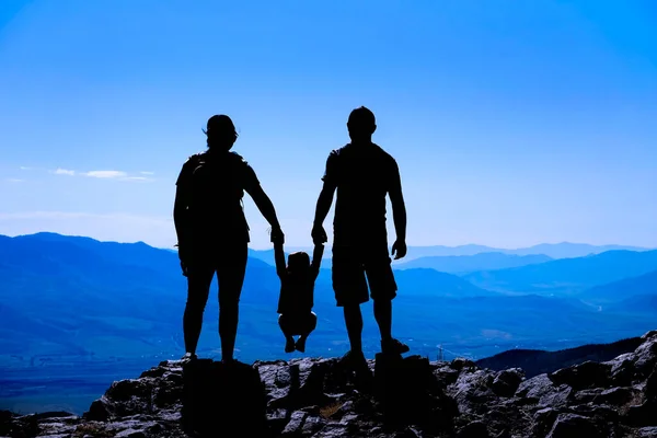 Rodzina Maluchem Szczycie Góry Sylwetka Trzymając Się Ręce Patrząc Góry — Zdjęcie stockowe