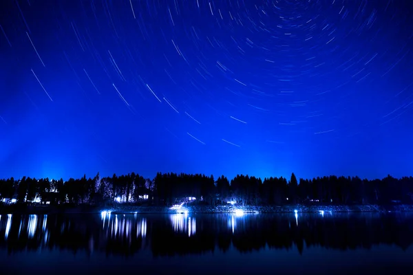 湖の夜空の星のトレイルと荒野の暗い光の円で松林 — ストック写真