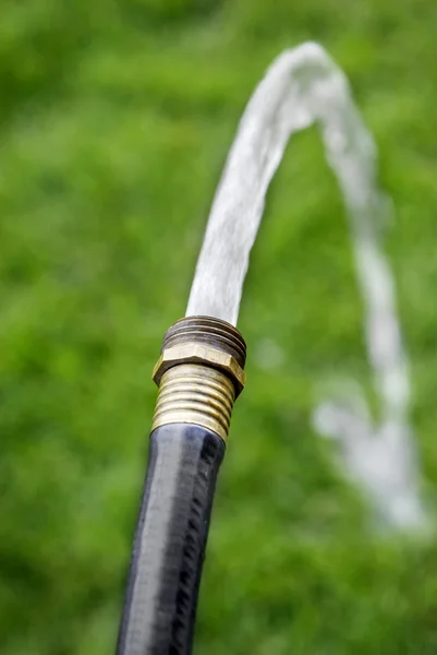 Schwarzer Schlauch spritzt Süßwasser auf Gras — Stockfoto