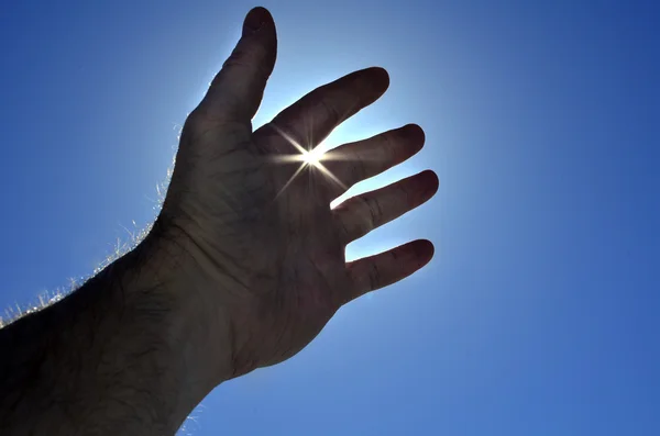 La mano della persona che raggiunge verso la luce del sole del cielo — Foto Stock