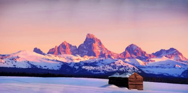 Teton Dağları 'nın görkemli manzarası. Kışın Sunset Light Grand Tetons. Tarladaki eski kulübe binası.