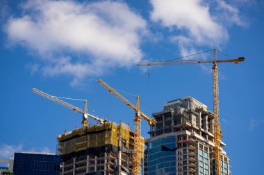Birçok bina yapım aşamasında ve mavi gökyüzünde vinçler var.