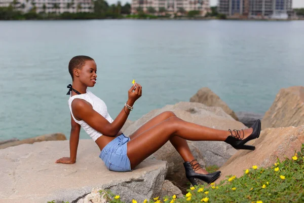 Mulher sentada em uma rocha e olhando para flores — Fotografia de Stock