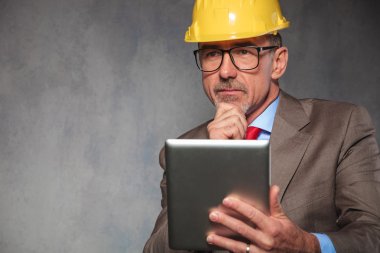 old engineer wearing glasses and helmet while thinking