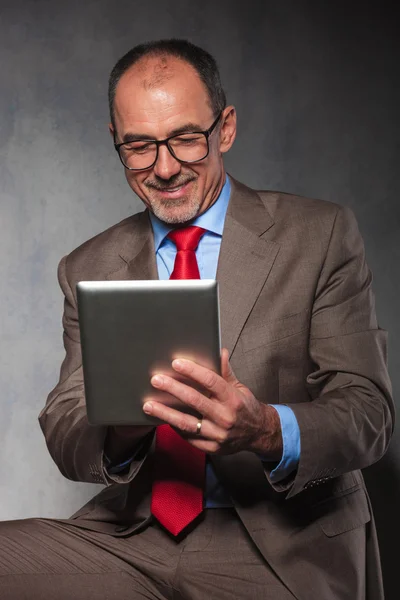 Handsome senior looking down at his tablet — Stockfoto
