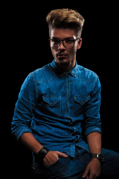 Beautiful man in denim seated with hand in pocket — Stockfoto