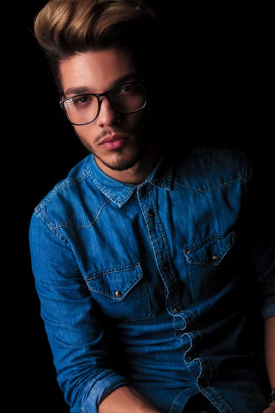 Casual young man in denim shirt posing in dark studio — Stok fotoğraf