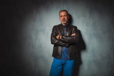 senior man in leather jacket posing in gray studio