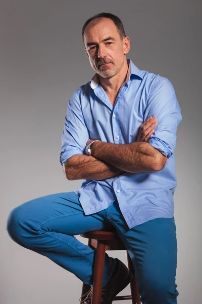 Зрілий сидячий випадковий чоловік в джинсах з схрещеними руками — стокове фото