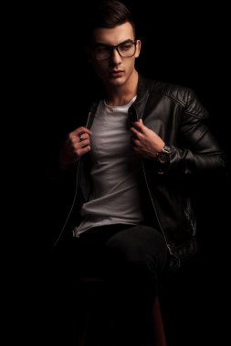 seated dark macho in black leather and glasses fixing jacket