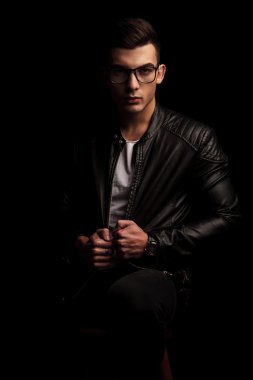 seated dark haired macho man in black leather wearing glasses