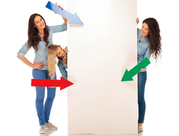 3 femmes occasionnelles pointant des flèches colorées vers un panneau d'affichage vierge — Photo