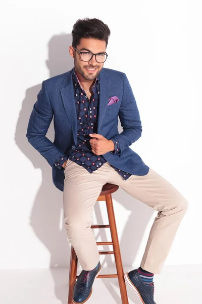 Happy young man in suit sitting with hand in pocket — Stock Photo, Image