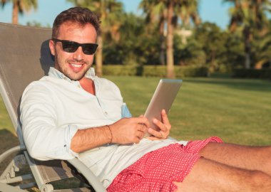 bir tablet pad bilgisayar tutan güneş gözlüklü adam oturmuş