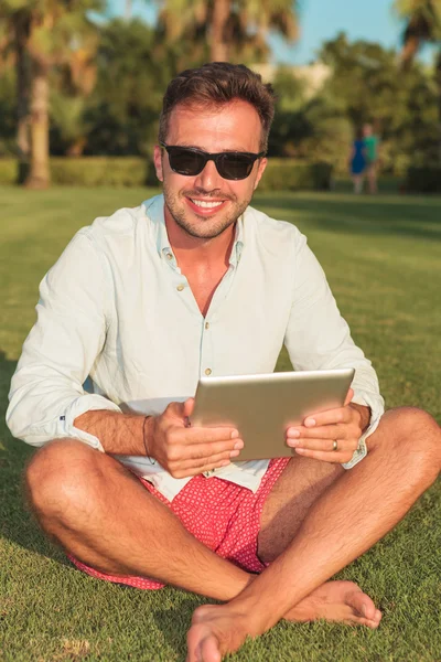 Jeune homme occasionnel assis sur le champ d'herbe tenant une tablette — Photo