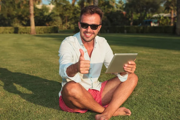 Чоловік сидить на траві на відкритому повітрі роблячи нормальні великі пальці вгору — стокове фото