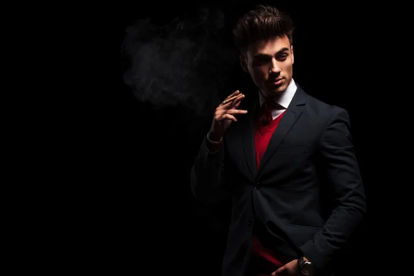 Elegant young businessman standing and smoking in studio — Stock Photo, Image