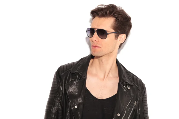 Модный мужчина в кожаной куртке и солнцезащитных очках смотрит в сторону — стоковое фото