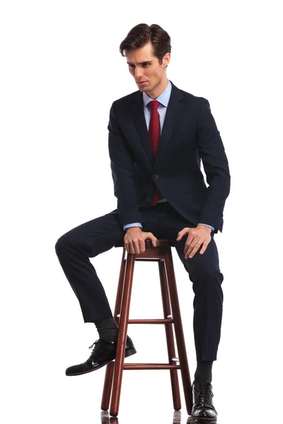 Geschäftsmann sitzt auf Hocker und blickt zur Seite — Stockfoto
