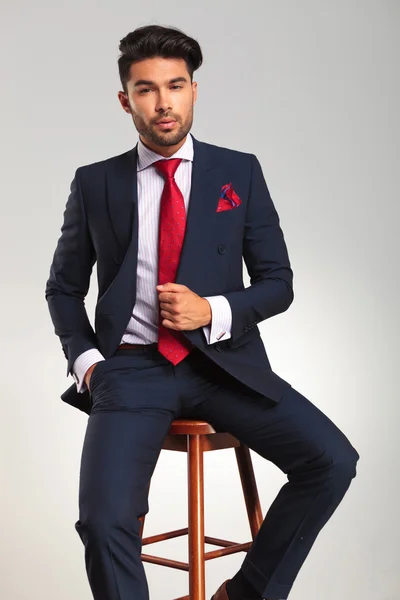 Elegante man in pak en stropdas zittend op een kruk — Stockfoto