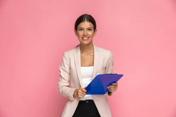 Vacker Affärskvinna Håller Blå Urklipp Och Ler Mot Rosa Bakgrund — Stockfoto