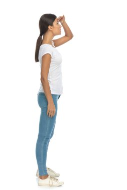 Beyaz stüdyo arka planında duran meraklı, sıradan bir kadının yan görünüşü