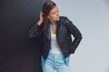 Moda modelinin siyah beyaz stüdyo arka planında dikilirken saçlarını düzeltip bakışlarını kaçırdığını düşünüyor.