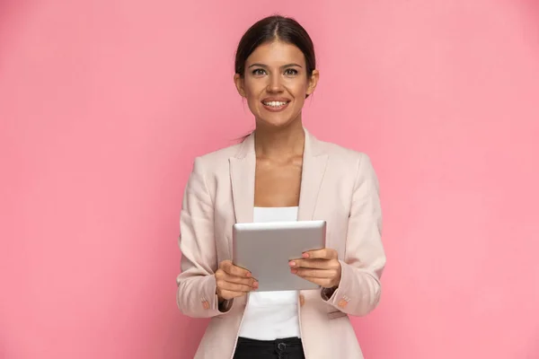 漂亮的女商人拿着平板电脑 带着粉红的背景对着摄像机微笑 — 图库照片