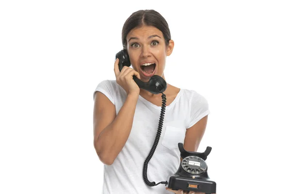 陽気なカジュアルな女性が古い電話で話していると笑っている間に白いスタジオの背景に立って — ストック写真