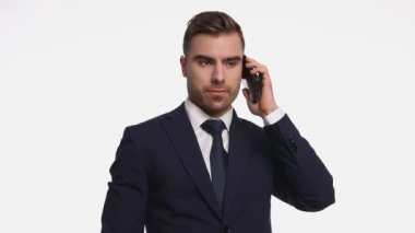 Lacivert takımlı gülümseyen genç adam telefonda konuşuyor ve parmaklıyor, stüdyoda beyaz arka planda tek başına duruyor.