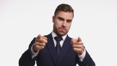 Lacivert takım elbiseli seksi genç işadamı, parmak işareti yapıyor, telefon jesti yapıyor ve stüdyoda beyaz arka planda gülümsüyor.