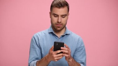 casual guy in jeans shirt answering, talking on the phone and laughing, making thumbs up gesture on pink background in studio
