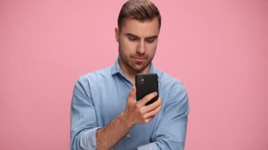 smiling young casual man in denim shirt talking on the phone, holding fist in the air and cheering on pink background