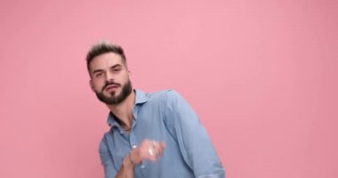 young casual guy dancing with great moves, gesturing crazy, kissing his finger gun and shooting on pink background