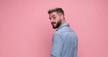 attractive casual man in rear view is turning around, feeling happily surprised and pointing at the camera on pink background